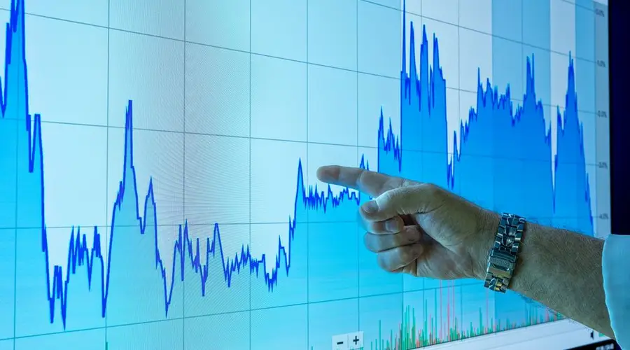 A hand points to a financial graph on a large screen, indicating market trends.
