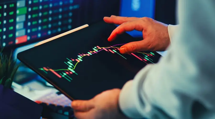 A close-up of a person using a tablet to analyze stock market trends and charts indoors.