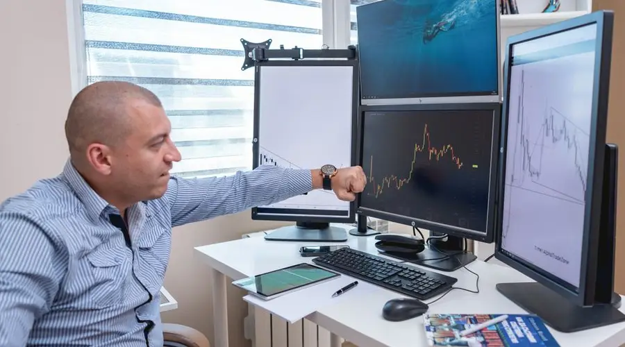 A trader analyzing market trends on multiple monitors at an indoor office desk.
