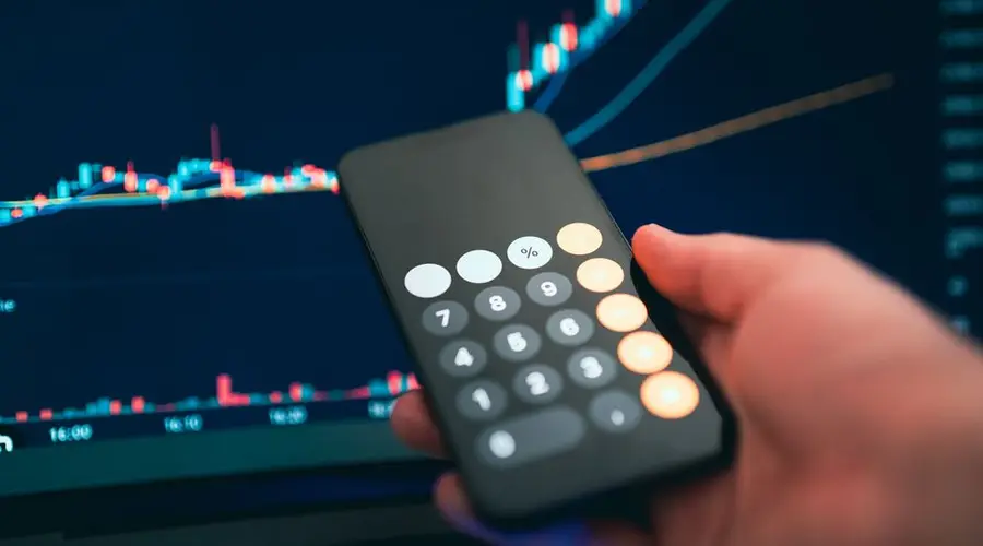 Close-up of a smartphone displaying a calculator with a financial chart in the background.