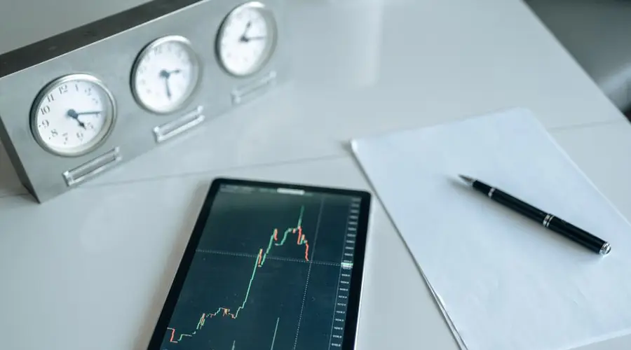 Tablet with stock market chart on a desk with clocks and pen.
