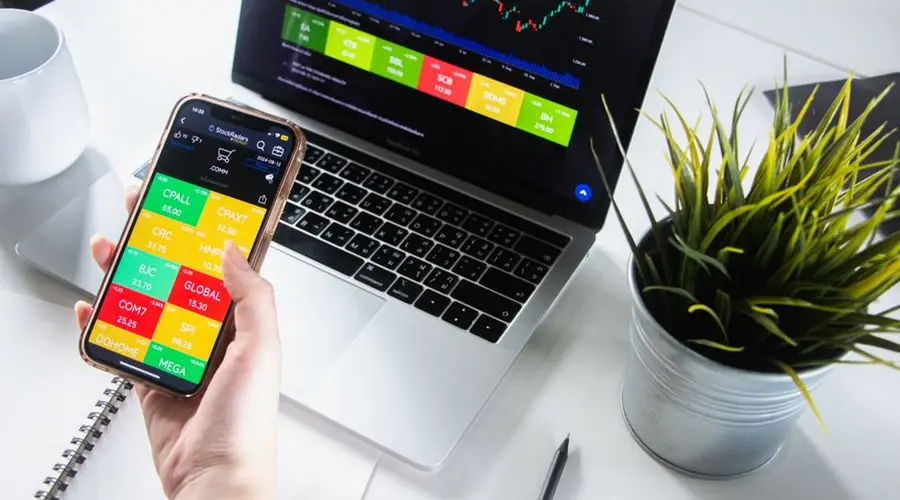 Person analyzing stock market trends on smartphone and laptop.