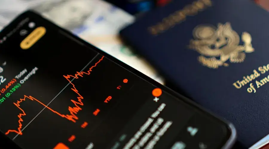 Close-up of a smartphone displaying stock data next to a US passport, suggesting travel and finance themes.
