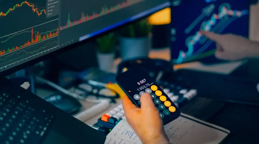 A focused shot of financial trading with screens, calculator, and data charts.