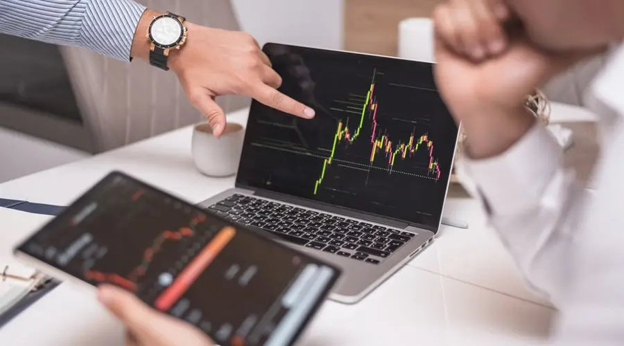 Business professionals analyzing cryptocurrency market trends on laptop and tablet.