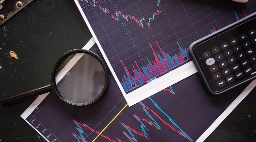 Stock market charts analyzed with a magnifying glass and calculator for financial research.