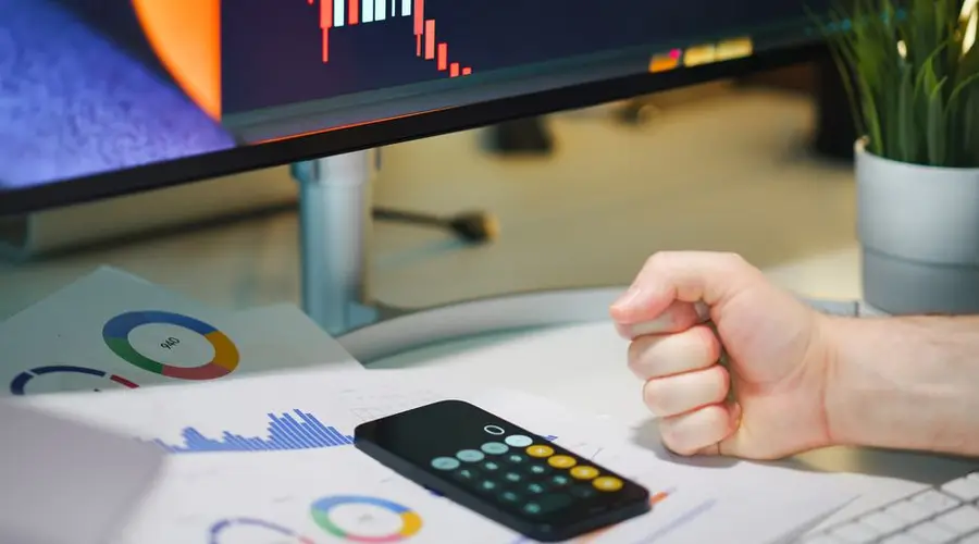 Close-up of a desk with financial graphs, a calculator, and a fist symbolizing determination.