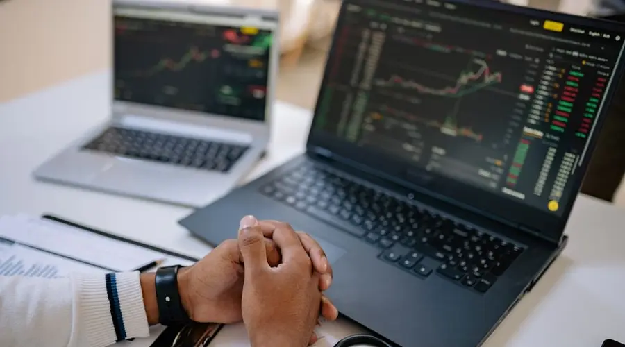Man seated at a desk using laptops to monitor stock market trends and investments.
