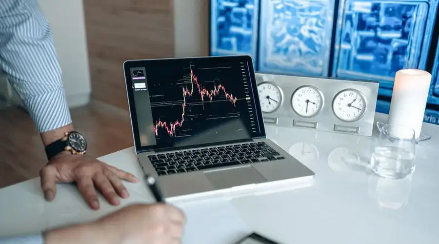 Person analyzing stock market graph on laptop in modern office setting with clocks and candle.