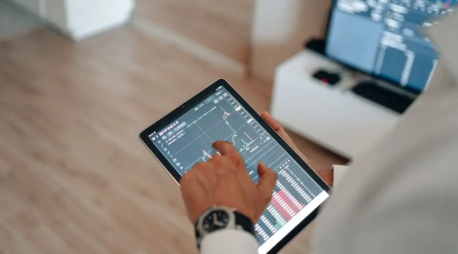 A person holding a tablet indoors displaying financial trading graphs, engaging in digital finance analysis.