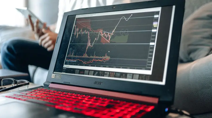 Close-up of a laptop displaying stock charts with a person in background.