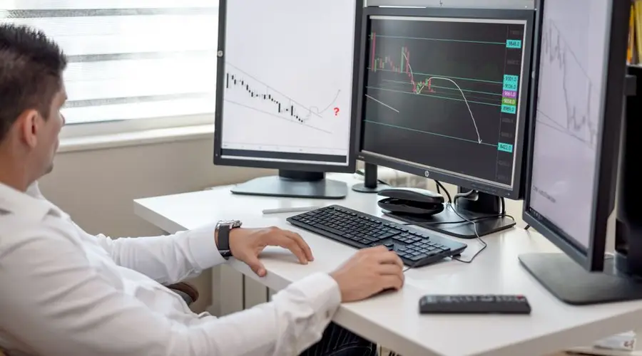 A businessman at his desk analyzing financial charts on multiple monitors.