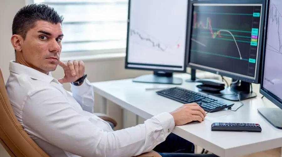 Professional stock market analyst monitoring data on multiple screens at a workstation.