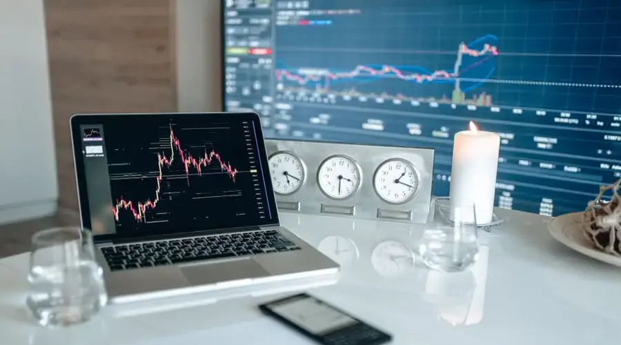A modern workspace featuring financial charts and multiple clocks on a white table, ideal for trading.