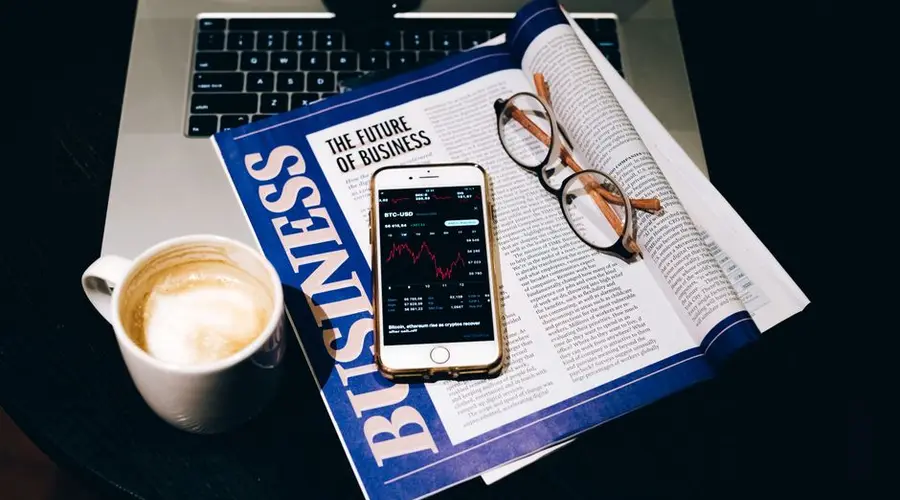A business setup with a laptop, coffee, phone, and newspaper. Perfect for finance themes.