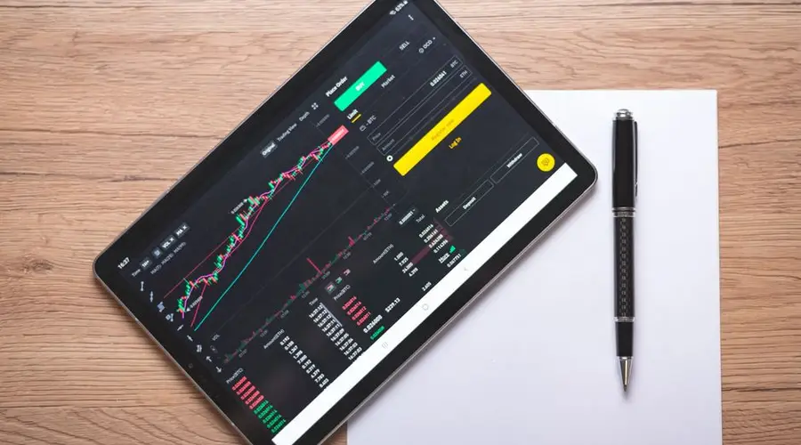 Overhead view of a digital tablet displaying stock market graphs and data on a wooden desk.