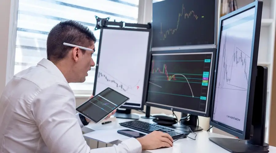 A man analyzing stock market graphs on multiple screens at a workstation.