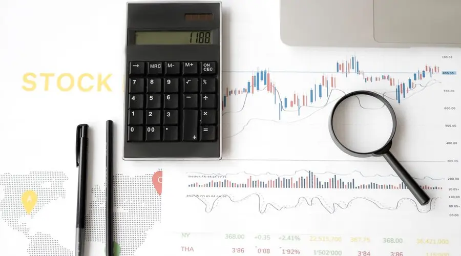 Flat lay of stock market analysis tools including calculator, graphs, and magnifying glass.