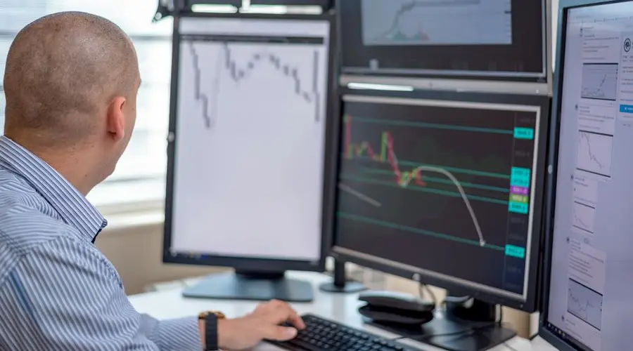 Trader analyzing financial data on multiple monitors in an office setting.