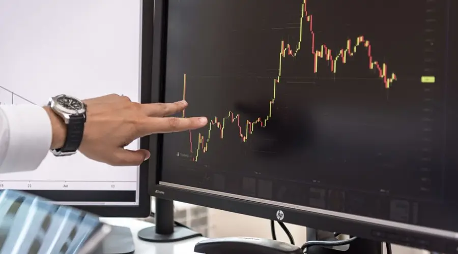 Detailed view of a hand pointing at a cryptocurrency trading graph on a monitor.