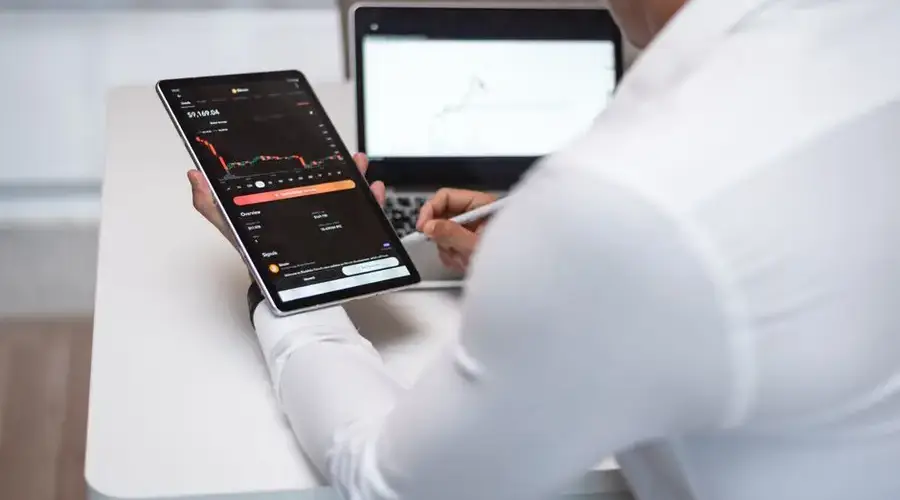 Businessman analyzing financial charts on tablet and laptop in modern office.