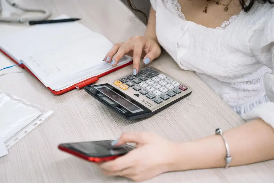 Close-up of a woman using a calculator and phone at her office desk.