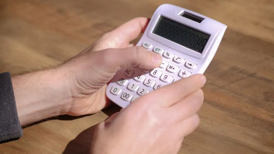 Hands using a pink calculator on a wooden table, emphasizing calculation and mathematics.