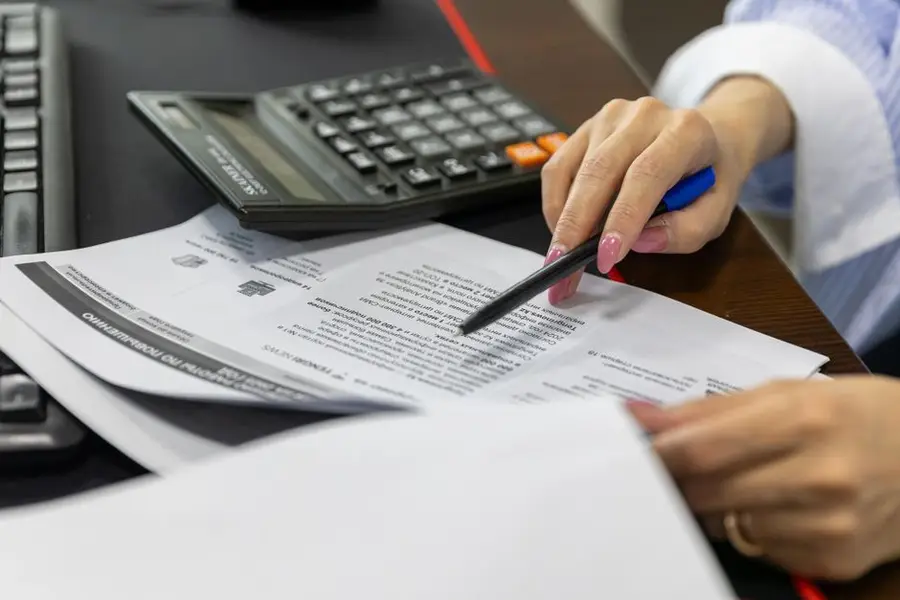 Close-up of a woman's hand reviewing financial documents with a calculator.