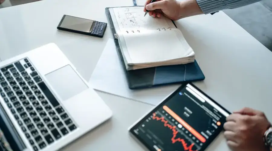 Person analyzing financial data on laptop, tablet, and notebook.