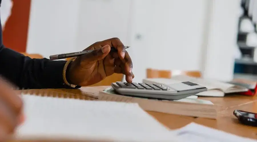 Close-up of a person using a calculator and pen for financial work at a desk.