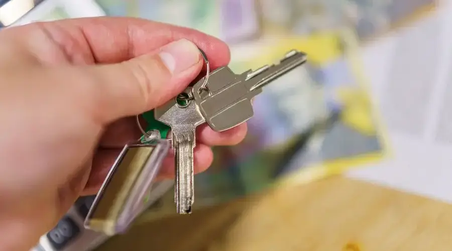 Close-up of keys in hand representing property ownership with blurred financial documents in the background.