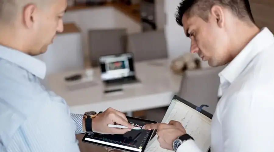 Two professionals reviewing financial charts on a tablet during a business meeting.