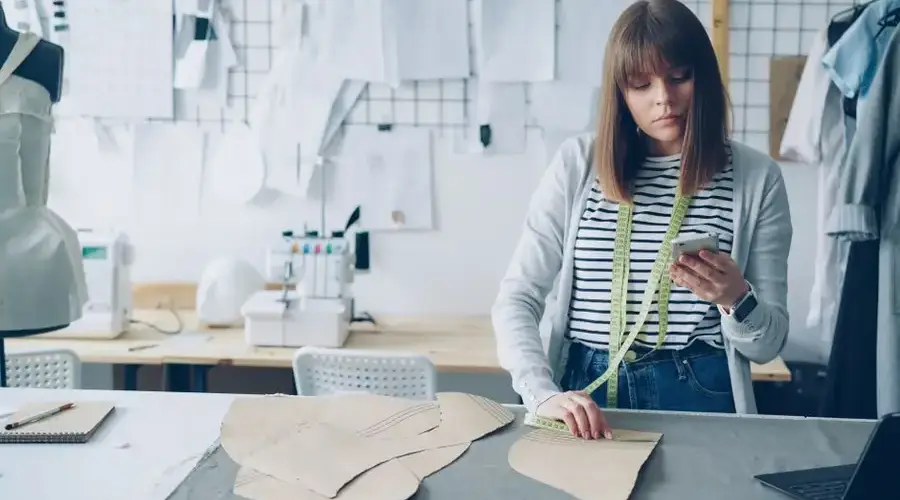 A fashion designer measures patterns in an organized studio with sewing tools.