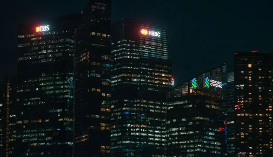 Illuminated city skyscrapers of major banks in Singapore's financial district at night.