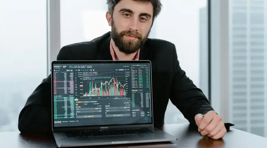 Businessman in office analyzing stock market trading data on a laptop screen.