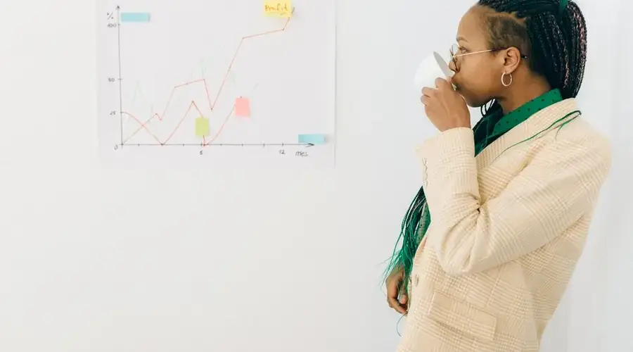 Professional woman in office attire drinking coffee while analyzing a financial graph indoors.