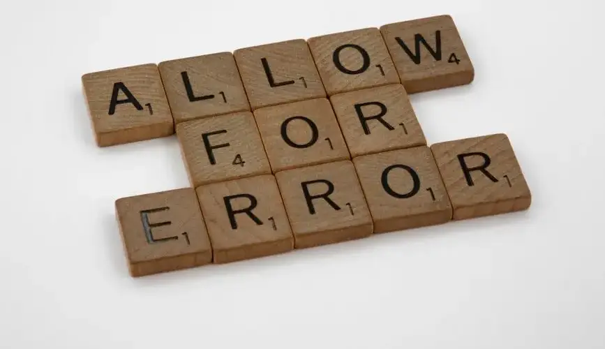Wooden Scrabble tiles spelling 'Allow for Error' on a white surface.