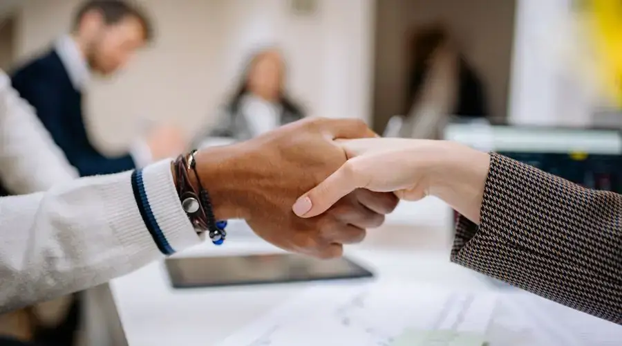 Diverse business professionals exchanging handshake in an office environment, symbolizing agreement.