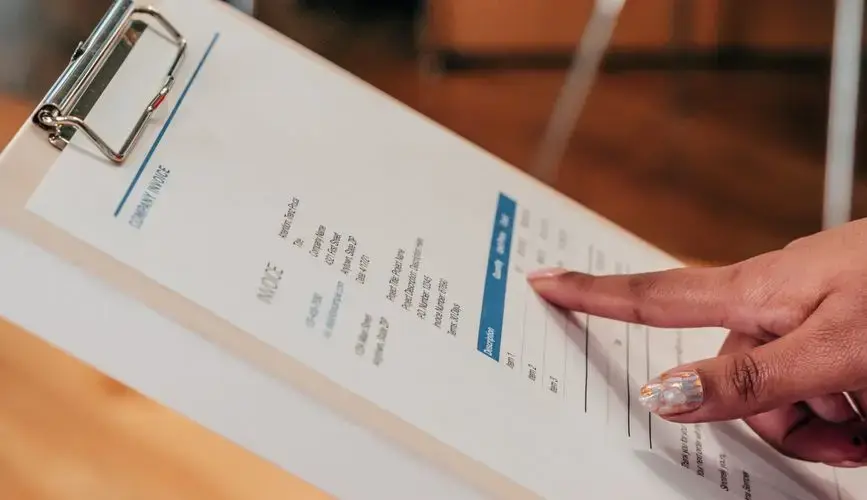 Close-up image of a person pointing to a document on a clipboard, indoors.