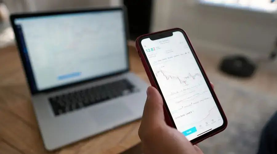 A person trading stocks on a smartphone and laptop. Ideal for finance themes.