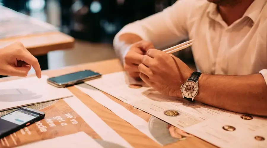 Two adults discussing a menu at a restaurant table with chopsticks and phones.