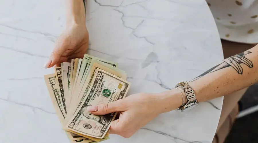 Hands holding and counting US dollar bills on a marble table, depicting wealth and finance.