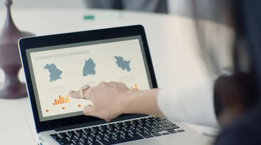 A woman pointing at a laptop screen showing a state comparison chart at a business desk.