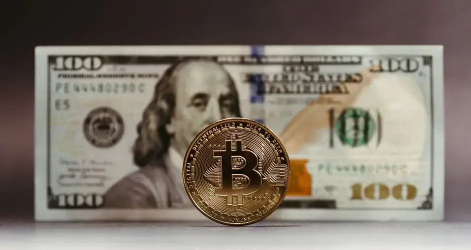 Close-up of a Bitcoin coin placed in front of a US hundred-dollar bill, highlighting cryptocurrency versus traditional money.