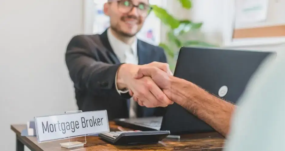Mortgage broker and client sealing a deal with a handshake in a bright, modern office.