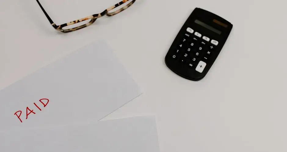Top view of financial papers labeled 'Paid' and 'Due' beside a calculator and glasses.