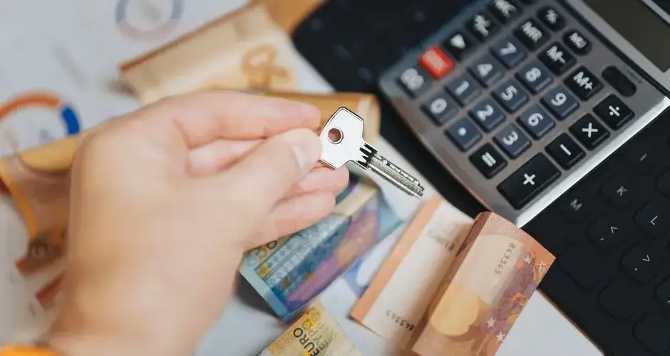 Hand holding key above Euro banknotes and calculator, symbolizing real estate investment.