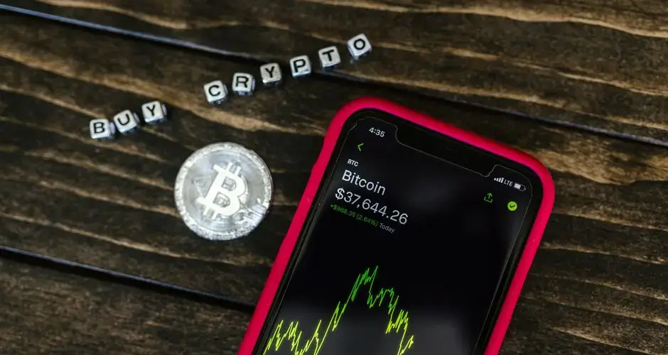 Smartphone showing bitcoin price with a physical coin and text representing cryptocurrency investment.