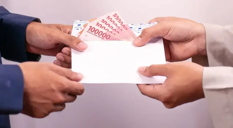 Hands exchanging an envelope with Indonesian Rupiah, highlighting financial transactions.