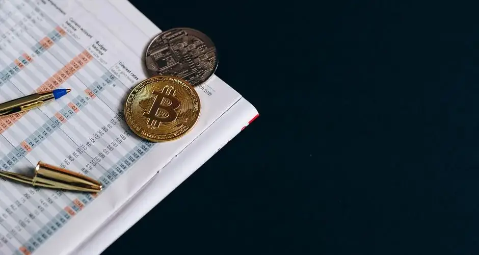 A close-up of Bitcoin with financial indicators and a pen on a black surface.